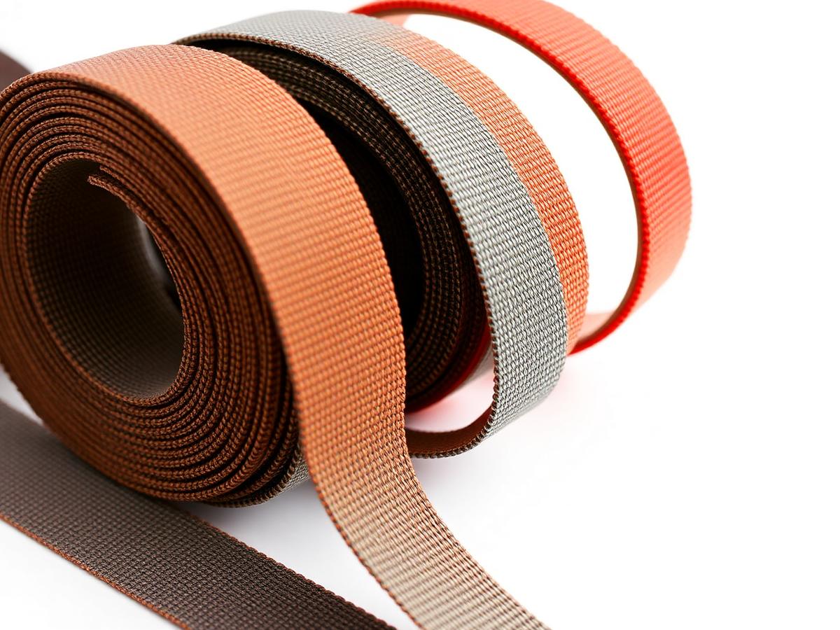Rolls of industrial woven webbing and technical tapes on a white background